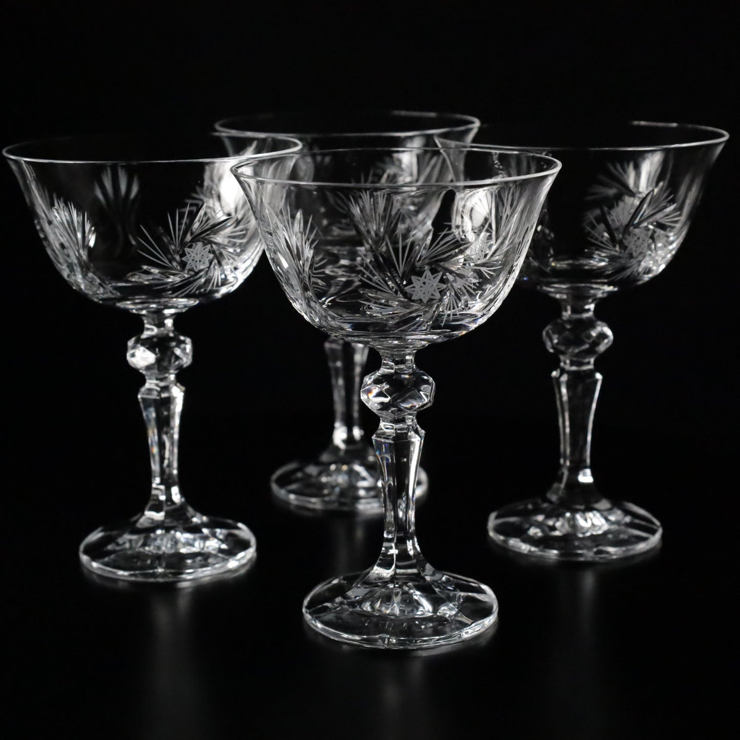 Set of intricately designed crystal stemware glasses with etched patterns, displayed on a reflective black surface.