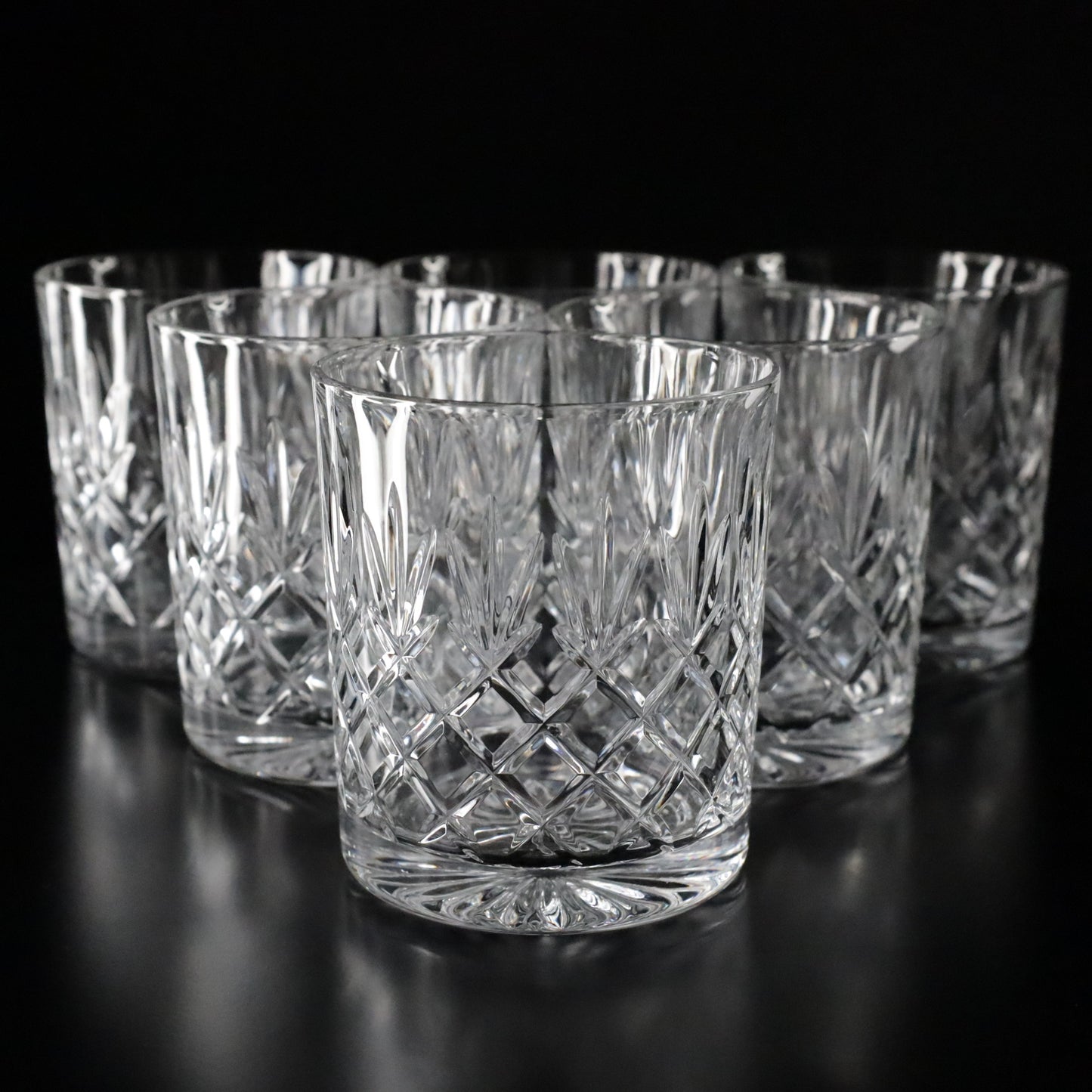 Elegant Crown crystal tumblers featuring intricate diamond-cut patterns, displayed as a complete set of six on a sleek black surface.