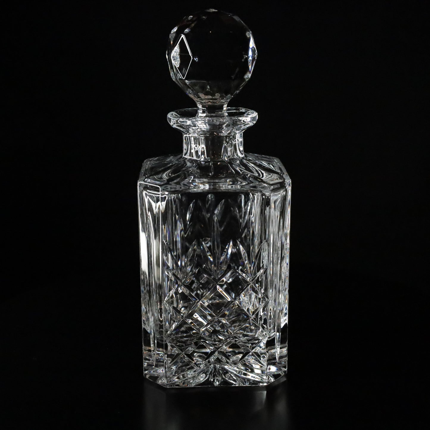 Elegant Crown crystal whisky decanter featuring intricate diamond-cut patterns and a faceted stopper, displayed on a sleek black surface.