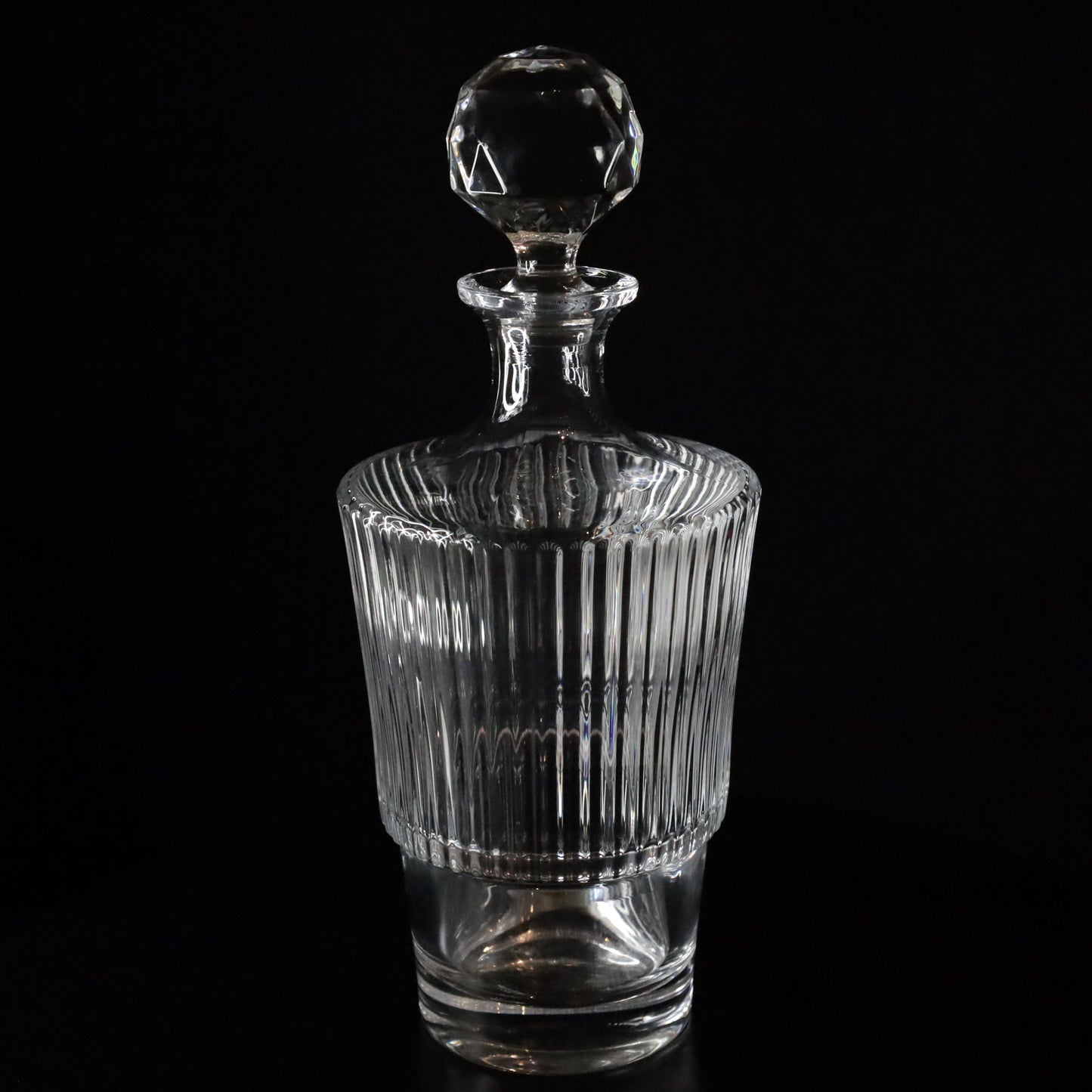 Elegant Serenity crystal wine decanter featuring vertical ribbed detailing and a faceted stopper, displayed on a sleek black background.