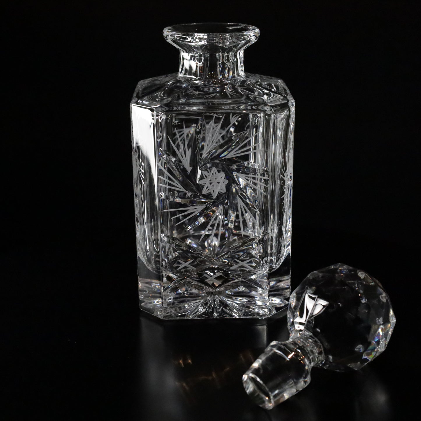 Sophisticated Antoinette crystal whisky decanter with ornate detailing and a geometric stopper, displayed on a sleek black surface.