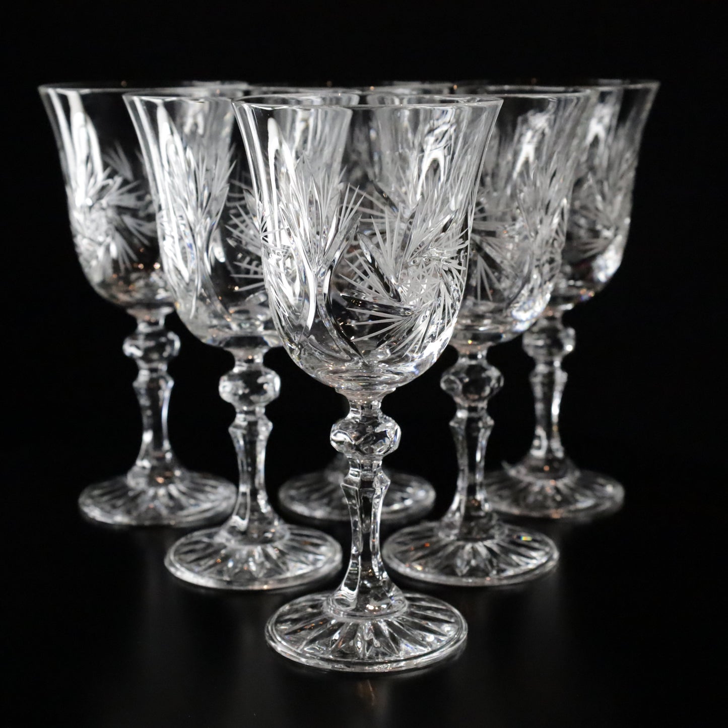 A sophisticated set of Antoinette crystal white wine glasses featuring intricate etched patterns and elegant stems, displayed on a sleek black surface.