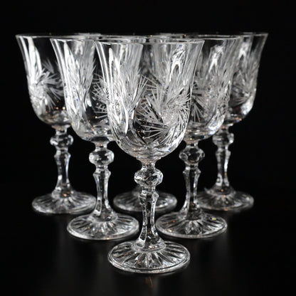 A sophisticated set of Antoinette crystal white wine glasses featuring intricate etched patterns and elegant stems, displayed on a sleek black surface.