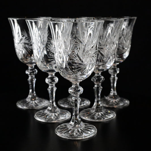 A sophisticated set of Antoinette crystal white wine glasses featuring intricate etched patterns and elegant stems, displayed on a sleek black surface.