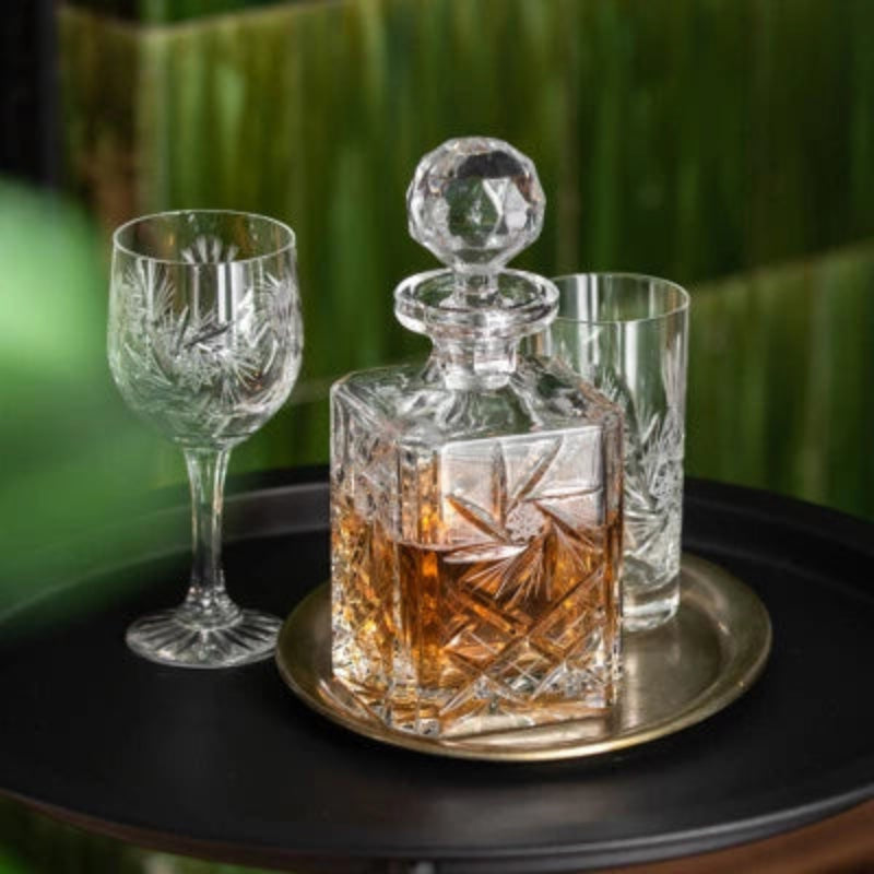 A crystal whisky decanter with a rectangular body featuring intricate starburst and geometric cut patterns, topped with a faceted, spherical stopper.